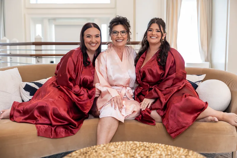 Stacy, Dean, and a third person sit on a beige sofa wearing burgundy and pink silk robes, smiling at the camera.
