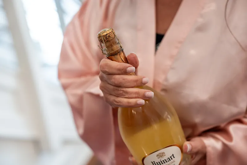 Someone in a pink shirt holds a champagne bottle with cork at The Plaza Suite.