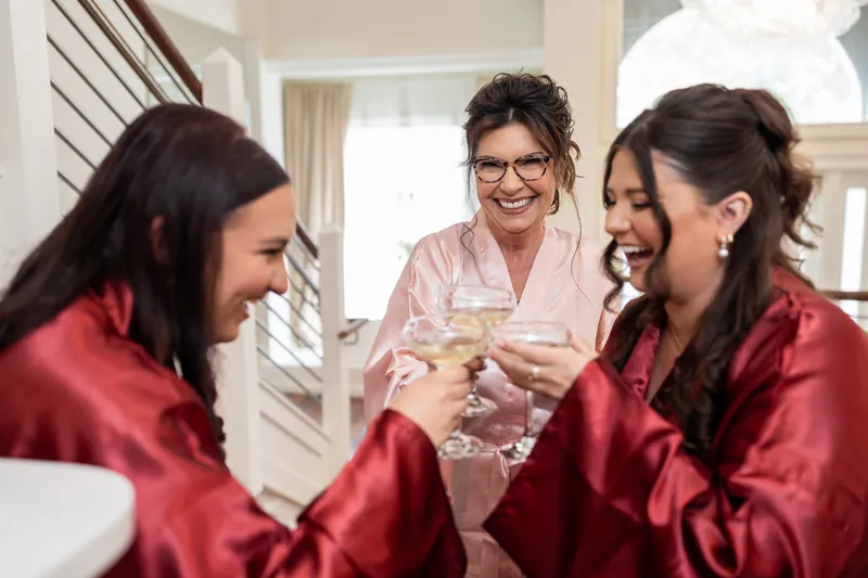 Three people in satin robes laugh together while holding champagne flutes indoors.