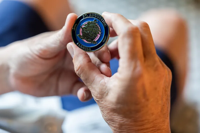 Hands hold a circular military-style challenge coin with blue and gold details.