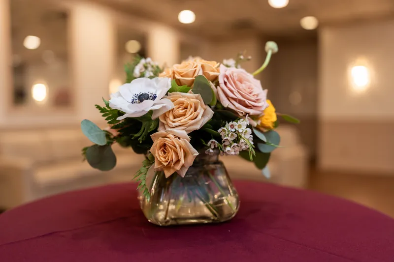 Peach, blush, and ivory roses arranged in a glass vase on a burgundy-draped table at The Treasury on the Plaza, St.