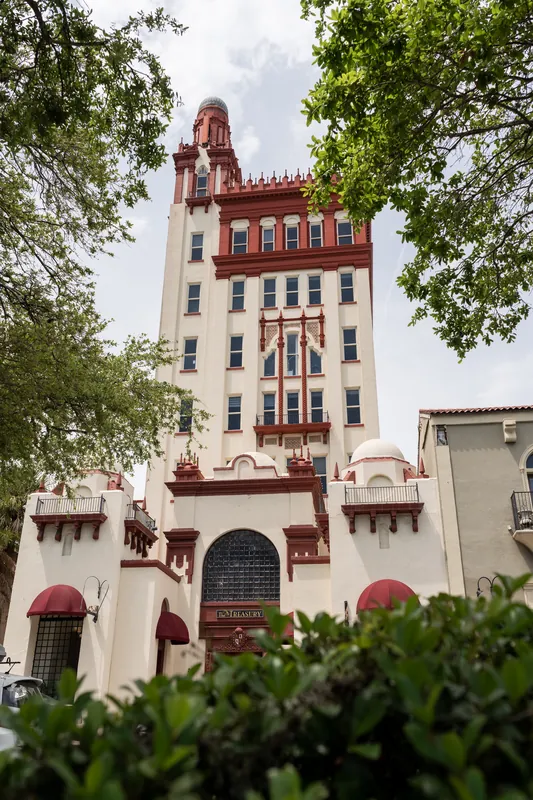 Red-brick historic building with crenellated tower framed by green foliage at The Treasury on the Plaza, St. Augustine.