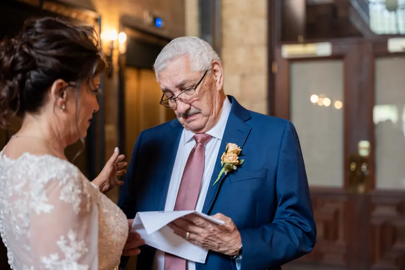 Dean reads from a card while exchanging vows with Stacy, who wears her lace gown in the historic venue's elegant interior.