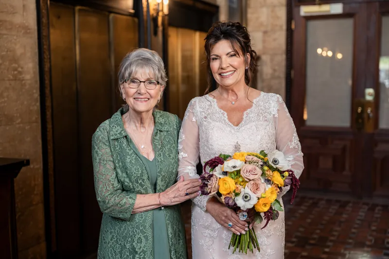 Stacy and an older woman in glasses stand together at The Treasury on the Plaza, both holding the vibrant mixed bouquet.