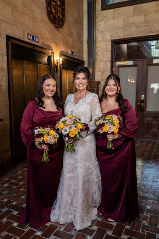 Stacy poses with two attendants in burgundy velvet at The Treasury on the Plaza's historic interior, each holding matching