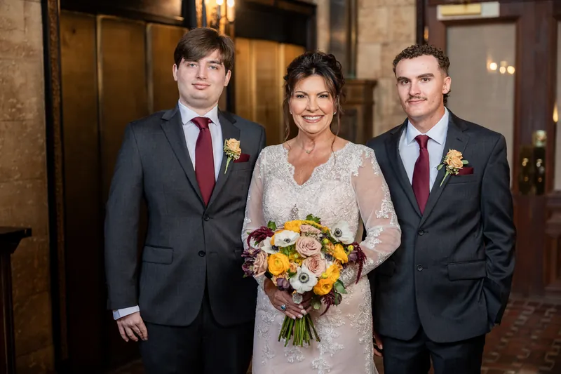 Stacy stands centered in her lace gown between two men in navy suits with burgundy ties at The Treasury on the Plaza.