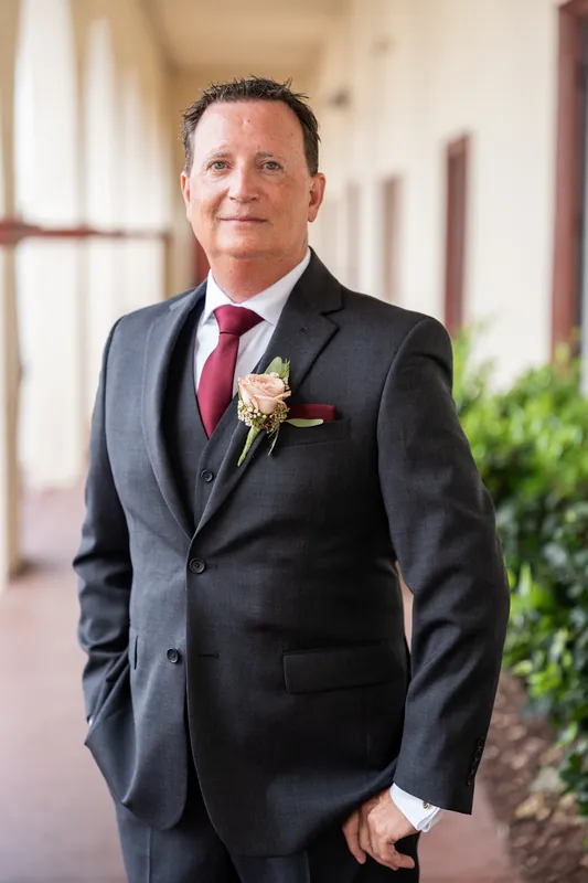 Dean poses in a charcoal suit with a boutonniere along the columned corridor at The Treasury.