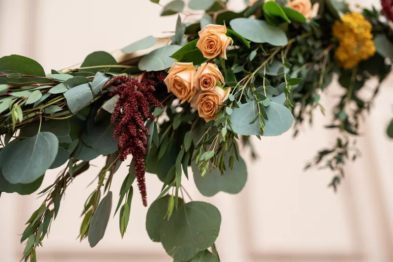 Orange roses, deep burgundy amaranthus, and eucalyptus greenery cascade in a decorative floral garland arrangement.