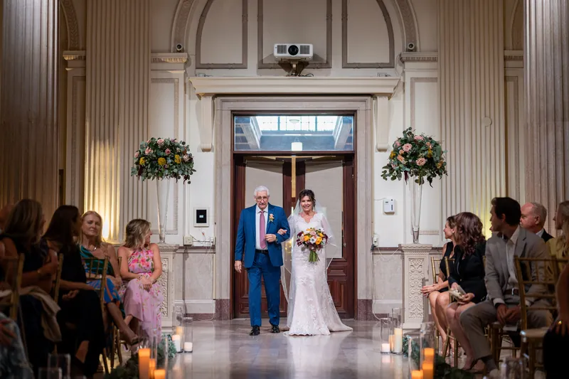 Stacy and Dean exchange vows facing each other under a marble archway lined with hanging floral arrangements and candles.