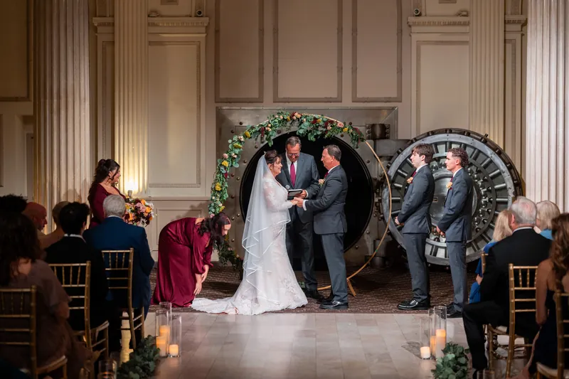 Stacy and Dean exchange vows before an ornate floral arch in the grand ballroom, flanked by family and guests in formal