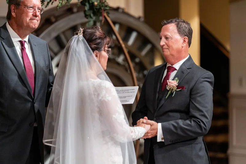 Dean holds Stacy's hand during their ceremony as an officiant stands nearby in the historic venue's elegant hall.