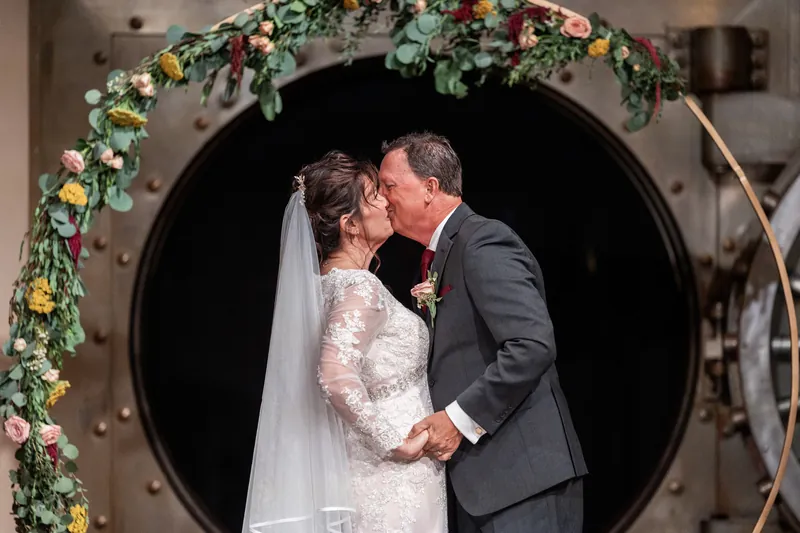 Stacy and Dean kiss beneath a floral arch at The Treasury on the Plaza, St. Augustine.