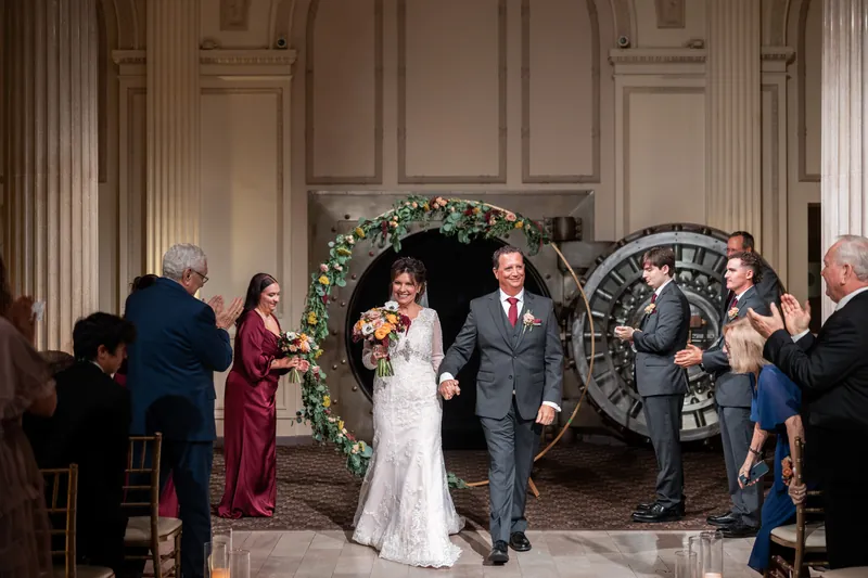 Stacy and Dean walk back down the aisle past guests in the grand columned ballroom.