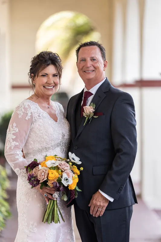 Stacy and Dean pose together in the colonnade, both smiling while holding their wedding bouquet.