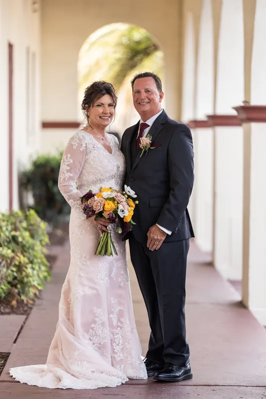 The couple walks hand-in-hand down the covered walkway lined with green trim and ivy-draped columns.