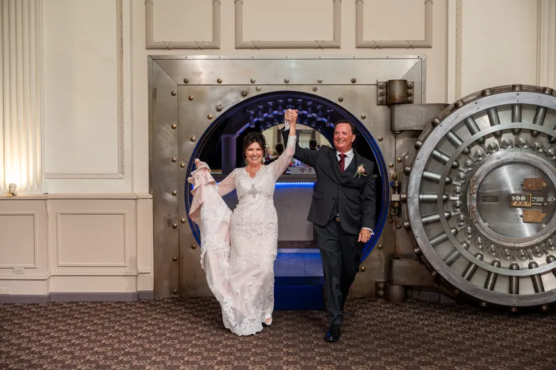 Stacy and Dean exit through a large decorative clock doorway while guests applaud around them.