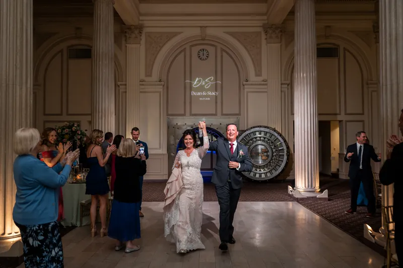 Stacy in her lace gown and Dean in his suit process through the columned hall as guests line both sides watching them pass.
