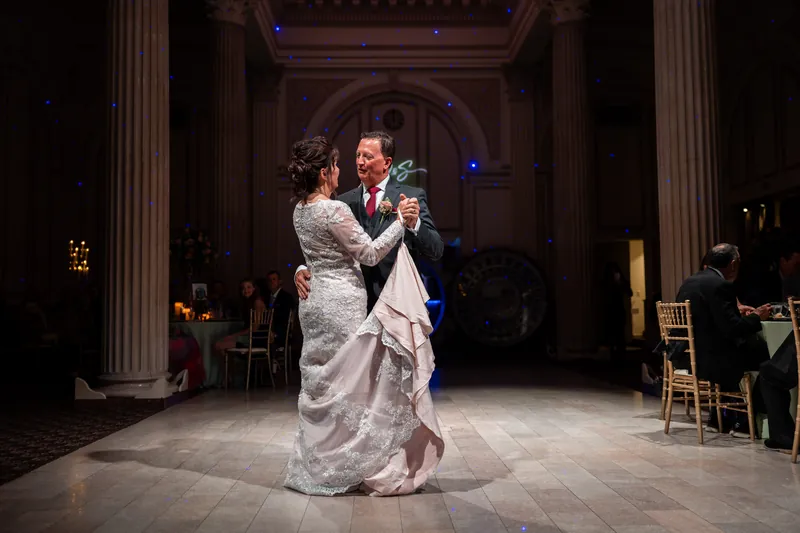 Stacy and Dean dance in the grand columned hall of The Treasury on the Plaza, her lace gown sweeping as he holds her close.