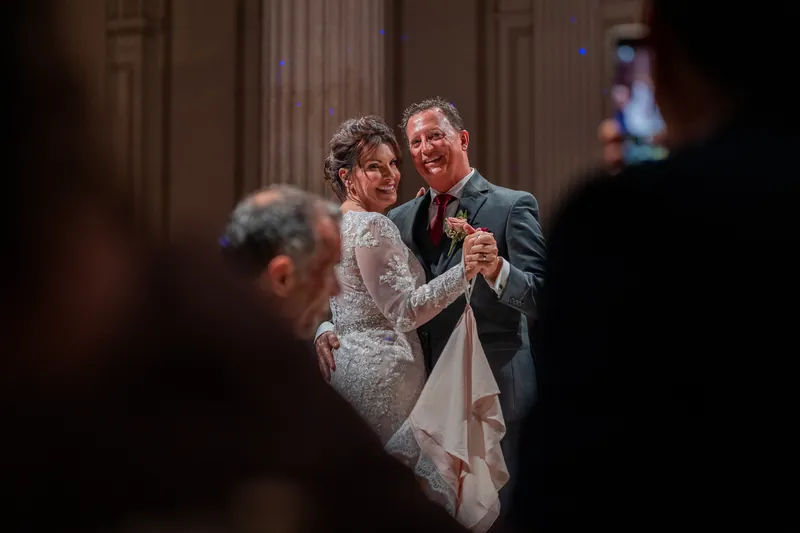 Guests watch from the foreground as Dean and Stacy move across the polished floor, their first dance unfolding before friends