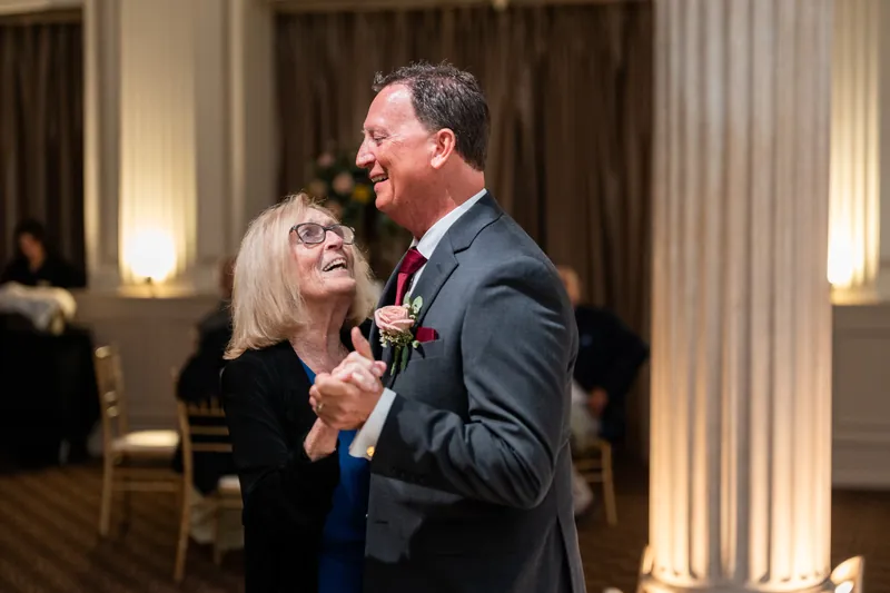 Dean shares a laugh with a woman in glasses and dark blazer, both holding microphones during the reception.