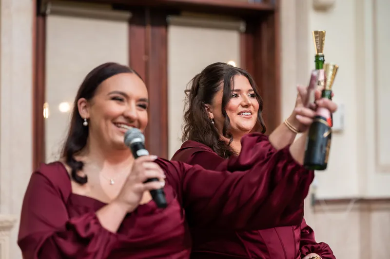 Two guests in burgundy velvet raise champagne bottles for a toast during the reception.