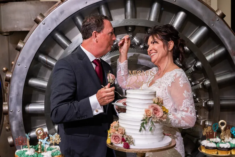 Stacy and Dean feed each other cake in front of a large industrial-style backdrop at their reception.