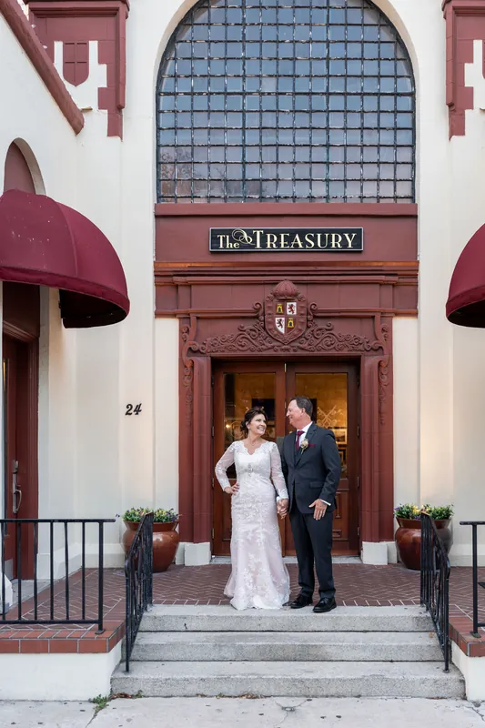 Stacy in her beaded gown and Dean in a dark suit stand in the grand arched doorway of The Treasury on the Plaza.