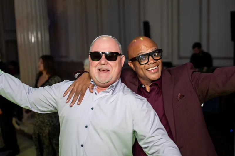 Two male guests smile broadly with their arms around each other's shoulders during the celebration.