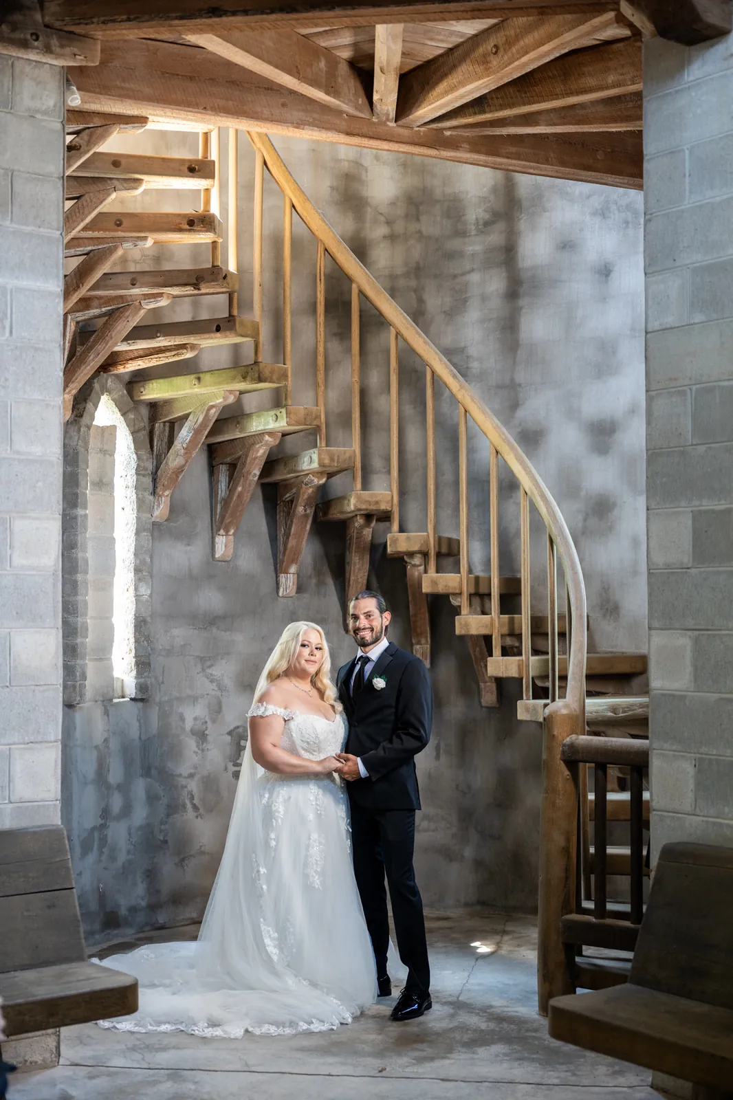 Ariel and Stephanie walk hand-in-hand beneath Castle Otttis's wooden spiral staircase with stone walls surrounding them.