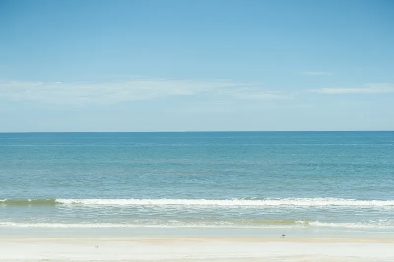 Calm Atlantic Ocean with gentle waves and sandy beach stretching across the horizon under clear blue sky.