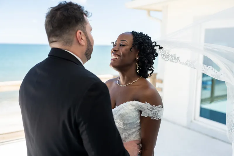 Stephen and Malika face each other by a window overlooking turquoise water at their St. Augustine Airbnb.