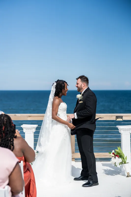 The couple gazes at each other while holding hands at the altar, ocean and horizon behind them.