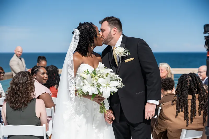 Stephen and Malika kiss as guests applaud around them on the oceanside deck in St. Augustine.