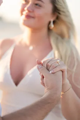 Paige holds Steve's arm and smiles at him while they stand among beach grasses with the waterway glowing behind them.