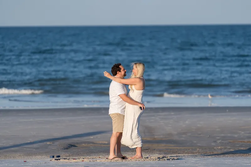 Steve and Paige embrace on the beach at Vilano, the ocean and waves visible behind them under afternoon light.