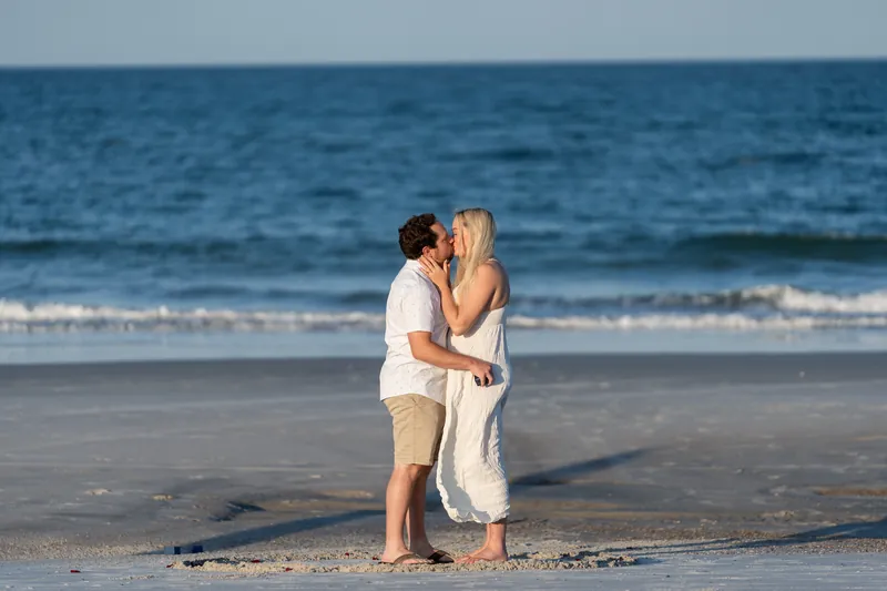 Steve and Paige kiss in the shallow water at Vilano Beach, their bodies close as small waves wash around them.