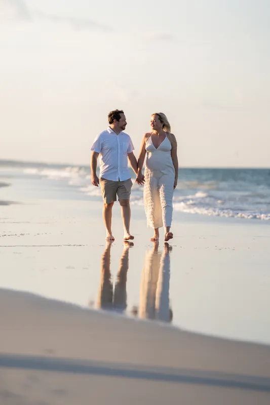 The couple holds hands while walking along the shoreline at Vilano Beach, their reflections visible in the wet sand below.