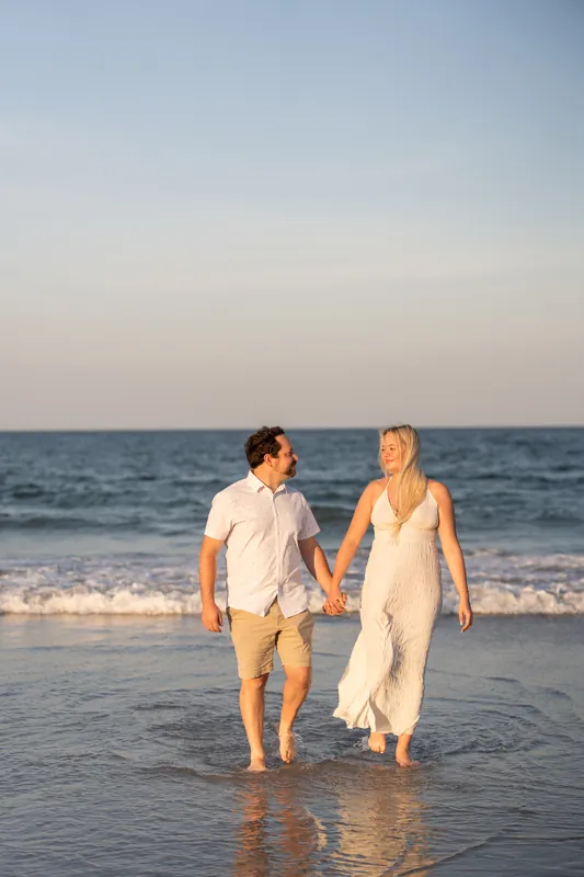 Steve in a light shirt and Paige in a flowing cream dress walk into the ocean at Vilano Beach.