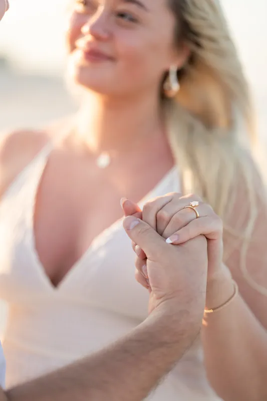 Paige displays her engagement ring at Vilano Beach, sunlit and smiling with ocean behind her.