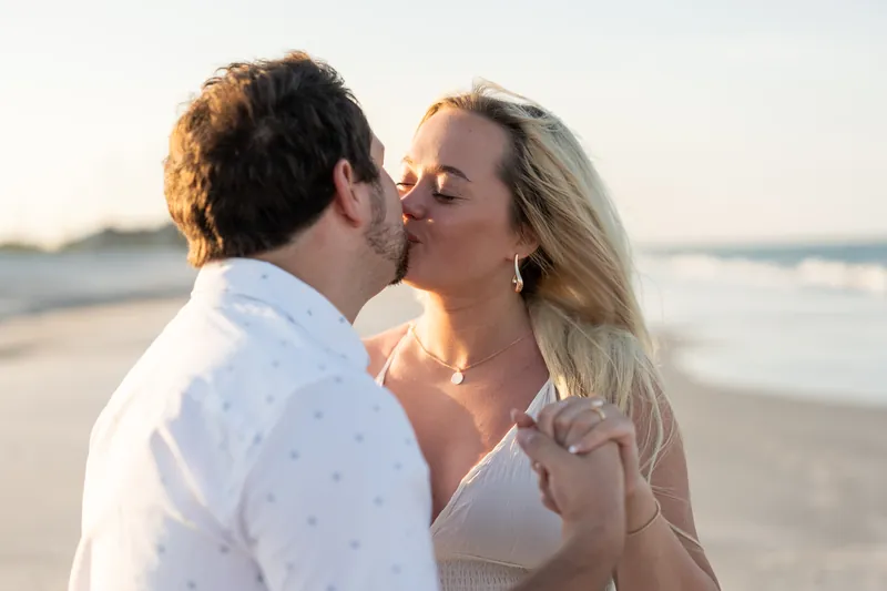 Steve kisses Paige on the beach as waves roll in at sunset.