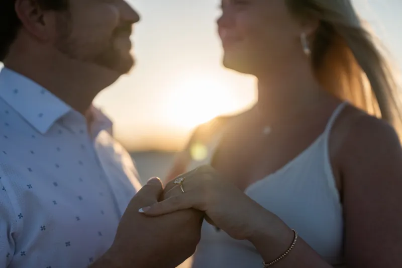 Steve and Paige's hands meet with the engagement ring visible against the glowing sunset.