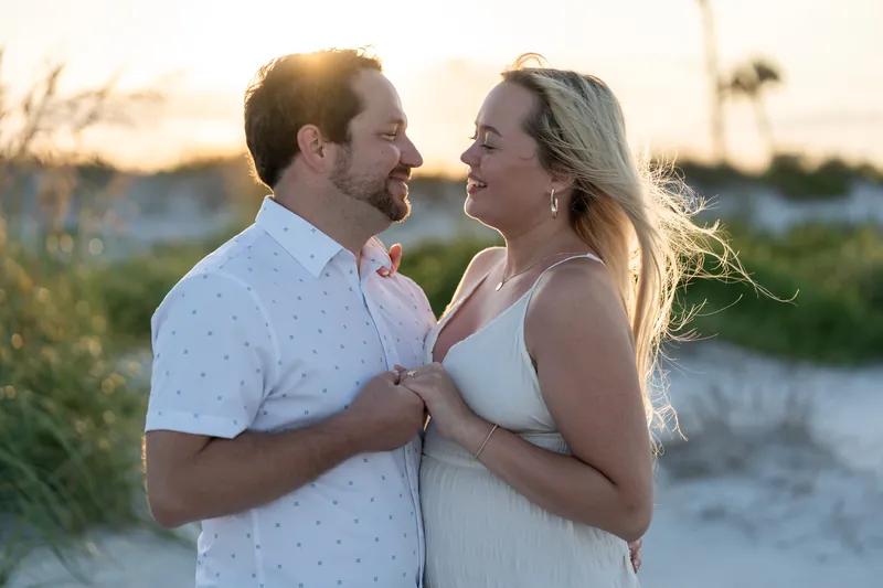 Steve and Paige hold hands at sunset on Vilano Beach with dunes glowing behind them.