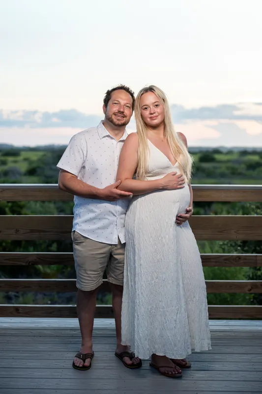 Steve and Paige stand together at a wooden railing overlooking Vilano Beach at sunset, both smiling at the camera.