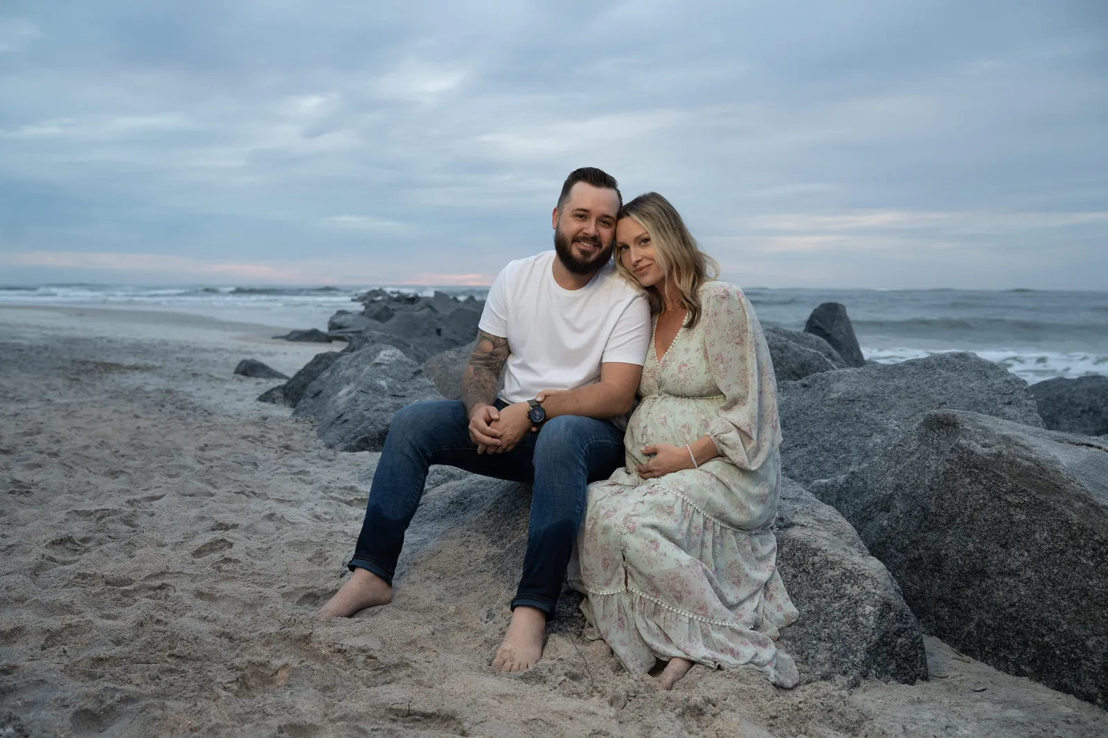 Expectant couple sits together on the jetty rocks at Vilano Beach during their sunrise maternity session.