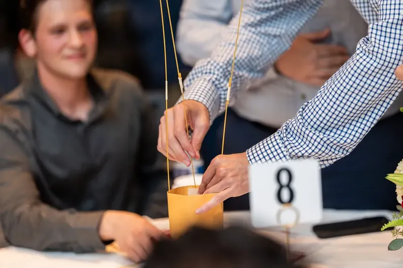 Hands position a straw into a drink at a numbered table during a group challenge or game.