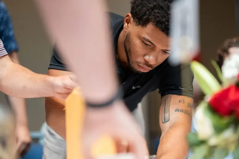 Man in dark shirt concentrates while manipulating a tall yellow object as part of a hands-on activity.