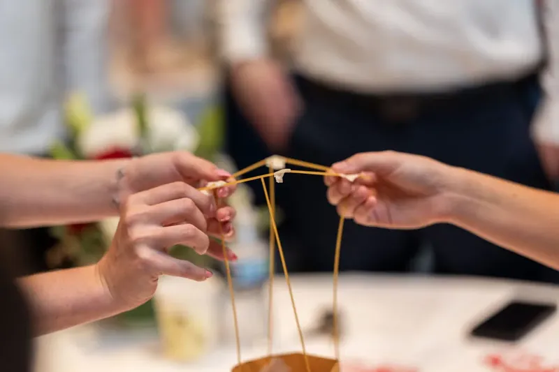 Two hands stretch golden string between them as part of an interactive team-building game or challenge.