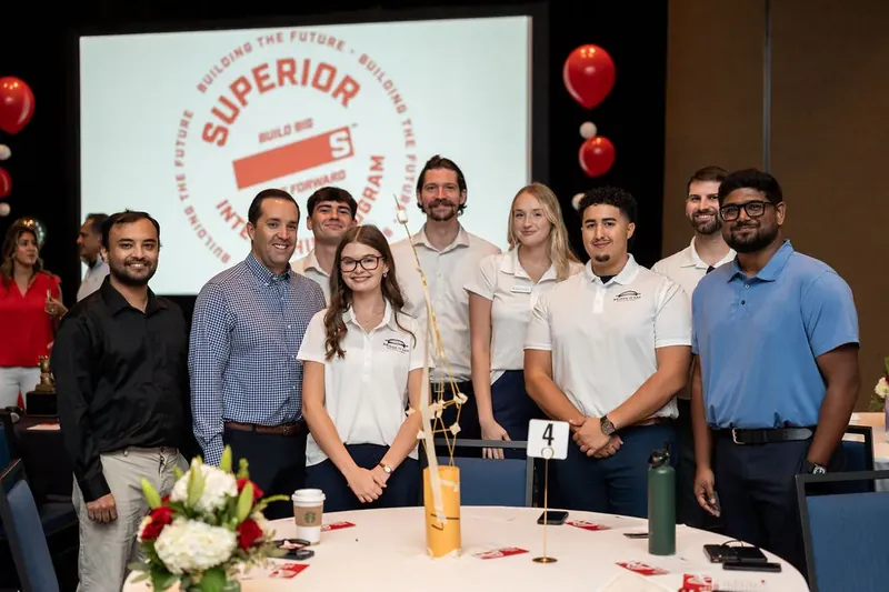 Team stands together in front of a Superior Party branded screen, holding lanyards and posing for a group photo