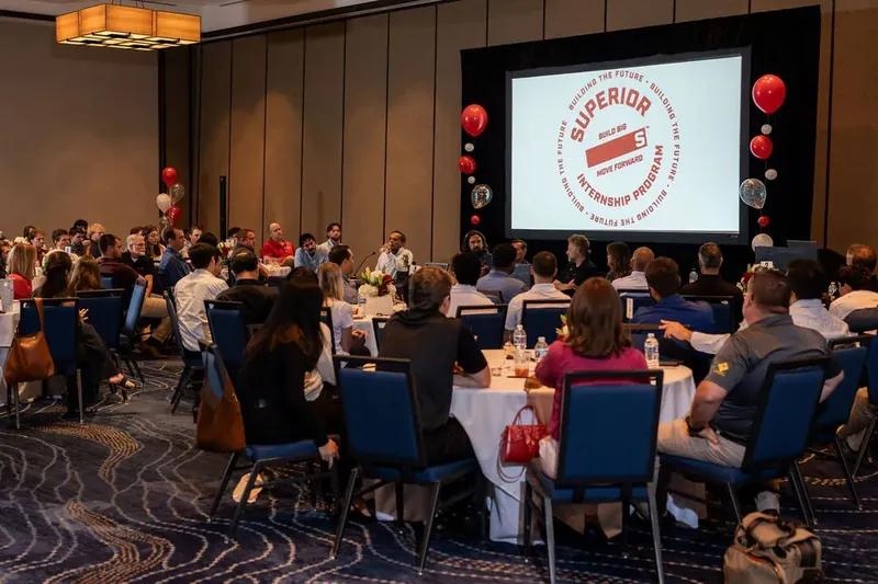 Corporate event attendees dine at round tables facing a projection screen displaying the Superior Party logo.