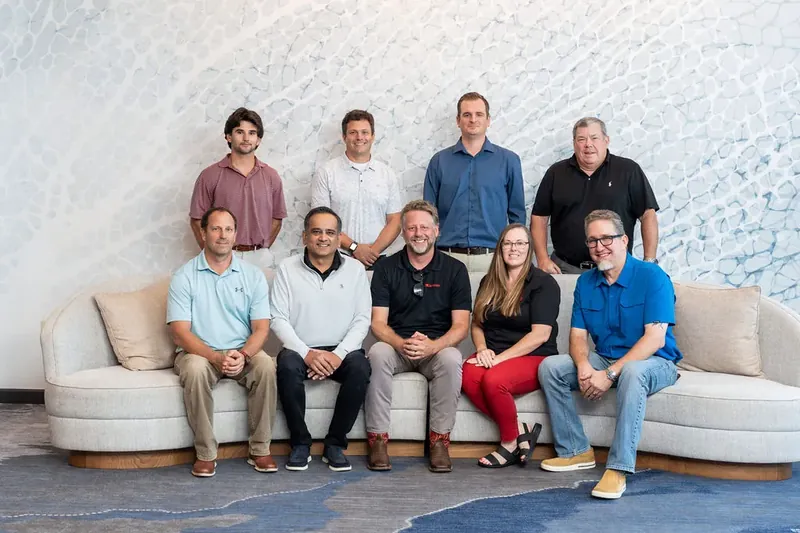Ten colleagues pose together on curved seating against an abstract blue-patterned wall.